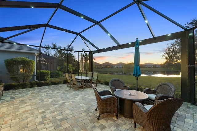 patio terrace at dusk featuring a lanai and a lawn