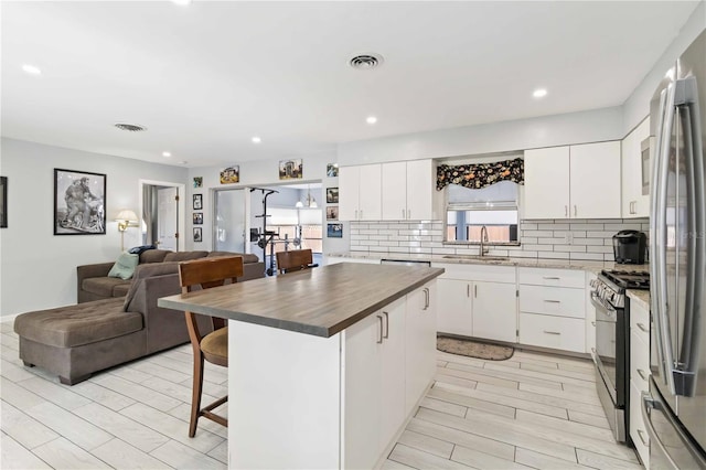 kitchen featuring appliances with stainless steel finishes, a center island, a kitchen breakfast bar, white cabinets, and sink