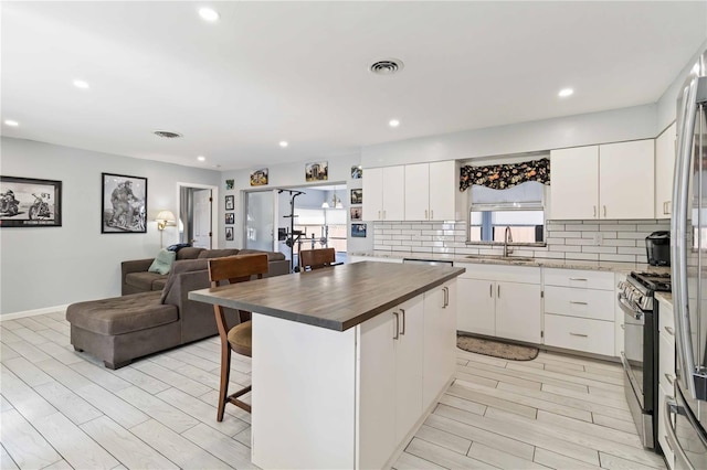 kitchen featuring a kitchen breakfast bar, stainless steel gas range, white cabinets, and a center island