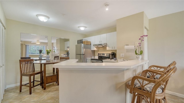 kitchen featuring light tile patterned flooring, a breakfast bar area, kitchen peninsula, stainless steel appliances, and white cabinets