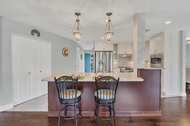 kitchen with appliances with stainless steel finishes, white cabinets, decorative light fixtures, and a kitchen island with sink