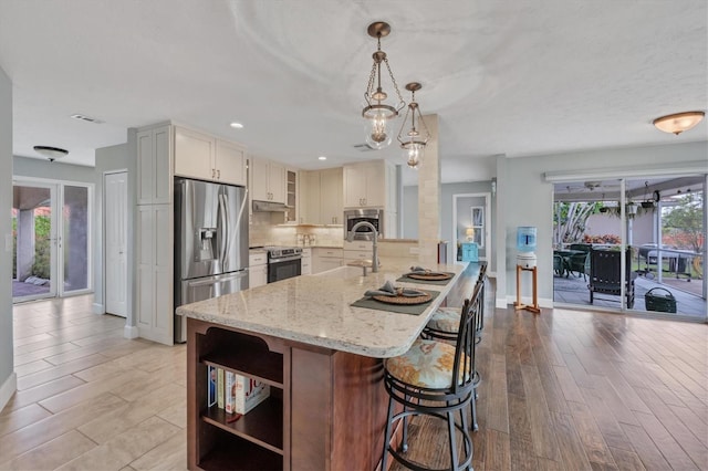 kitchen featuring light stone countertops, decorative light fixtures, stainless steel appliances, tasteful backsplash, and a breakfast bar