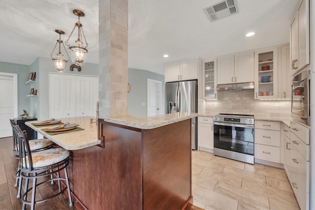 kitchen featuring decorative light fixtures, white cabinetry, appliances with stainless steel finishes, a breakfast bar area, and light stone counters