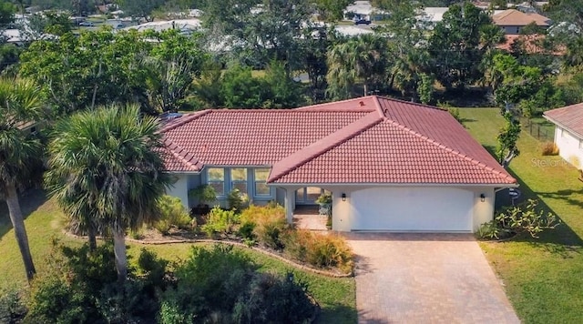 mediterranean / spanish house with decorative driveway, a front lawn, a tiled roof, a garage, and stucco siding
