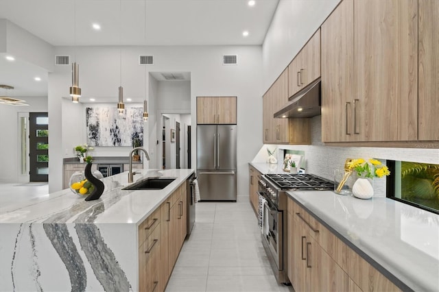 kitchen with backsplash, sink, high quality appliances, hanging light fixtures, and light stone counters