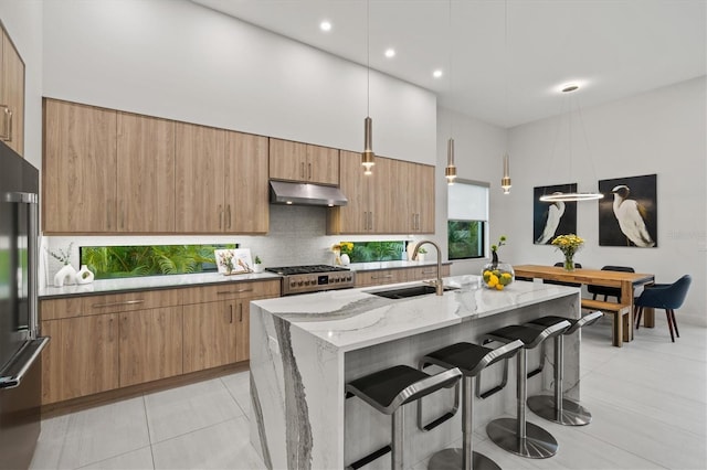 kitchen featuring a center island with sink, sink, hanging light fixtures, light stone counters, and range