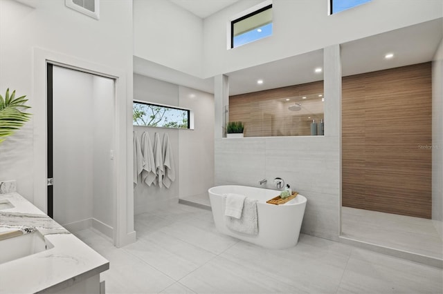 bathroom with a high ceiling, independent shower and bath, tile walls, tile patterned floors, and vanity