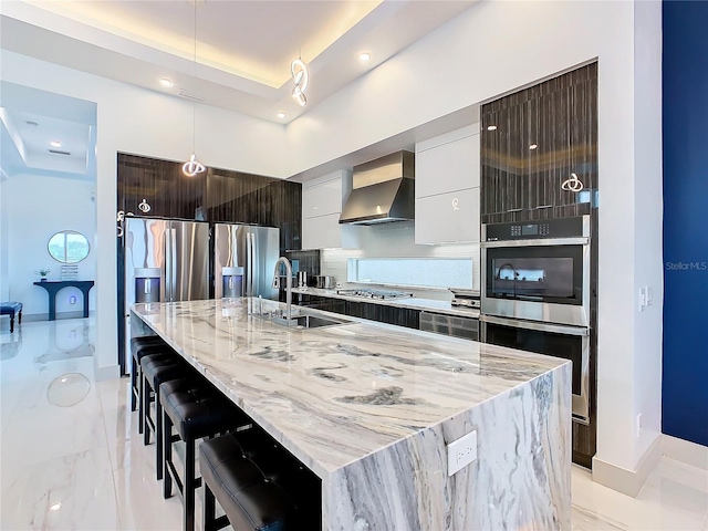 kitchen with a kitchen breakfast bar, appliances with stainless steel finishes, wall chimney exhaust hood, a kitchen island with sink, and sink