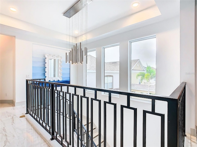 hall featuring a tray ceiling, an inviting chandelier, and a wealth of natural light