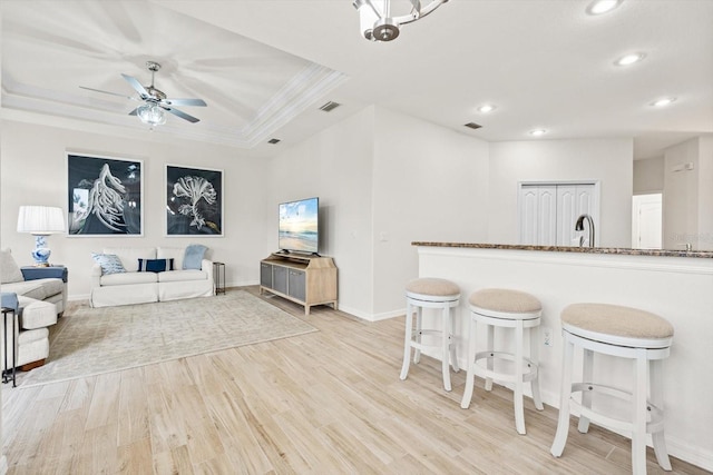 kitchen featuring ornamental molding, a tray ceiling, light hardwood / wood-style floors, and a kitchen bar