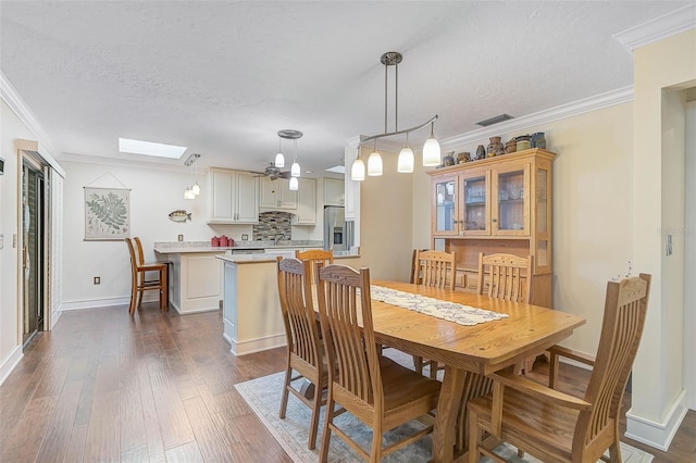 dining area with a textured ceiling, dark wood-type flooring, crown molding, and a skylight