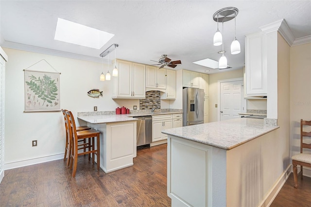 kitchen featuring a skylight, stainless steel appliances, a kitchen breakfast bar, kitchen peninsula, and decorative light fixtures