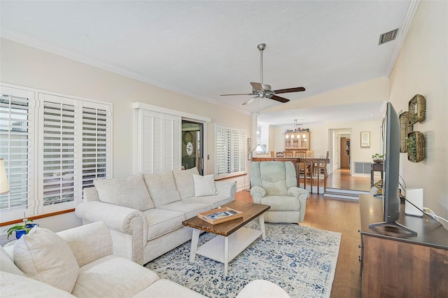 living room featuring vaulted ceiling, crown molding, light hardwood / wood-style floors, and ceiling fan with notable chandelier