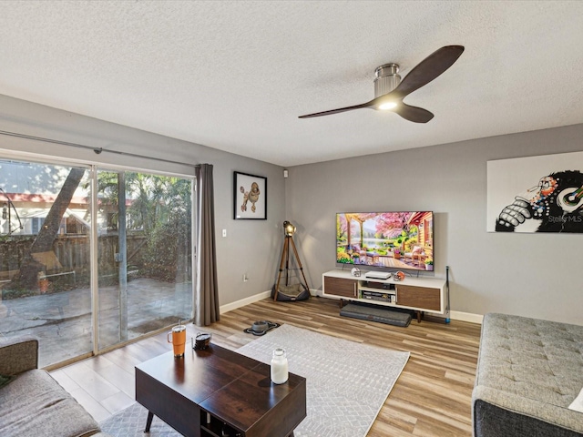 living area featuring a ceiling fan, baseboards, light wood finished floors, and a textured ceiling