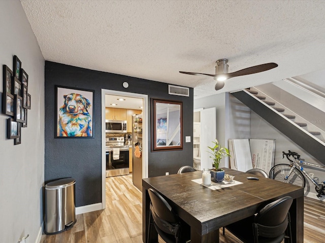 dining room with light wood-type flooring, visible vents, a textured ceiling, baseboards, and stairs