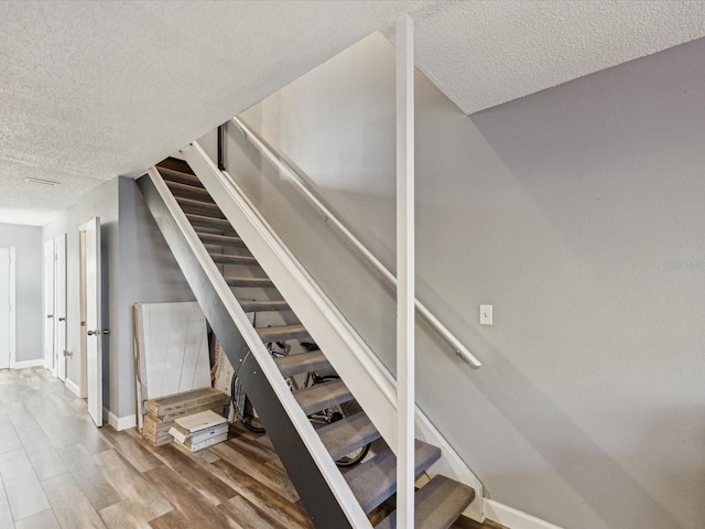 stairs featuring a textured ceiling, baseboards, and wood finished floors