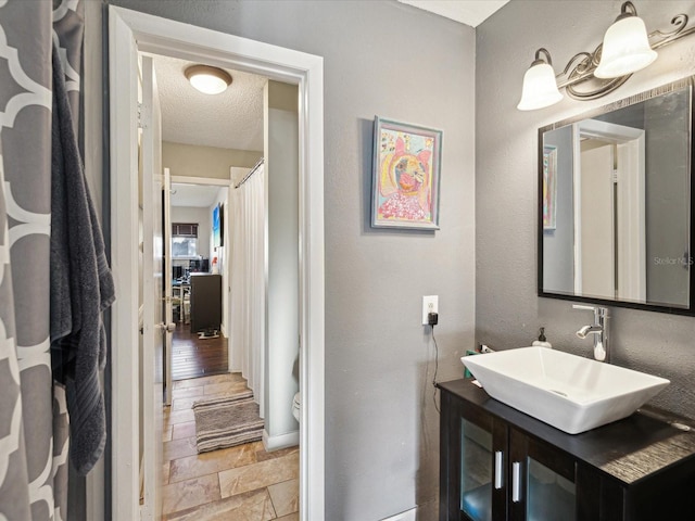 bathroom featuring vanity, toilet, a textured wall, and a textured ceiling