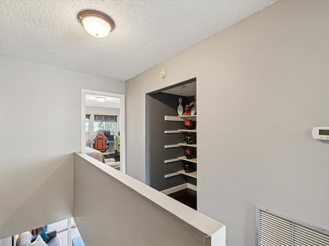 corridor with an upstairs landing, visible vents, and a textured ceiling