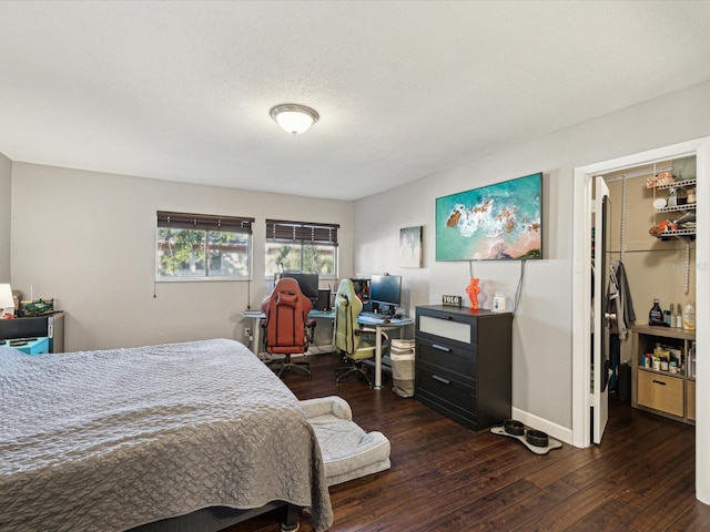 bedroom with baseboards, wood-type flooring, a textured ceiling, and a spacious closet