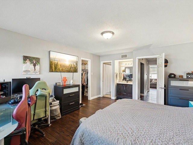 bedroom with visible vents, a walk in closet, baseboards, dark wood finished floors, and a closet