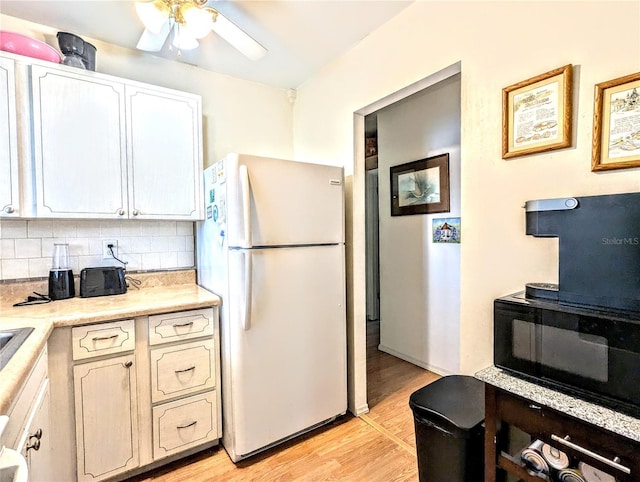 kitchen featuring decorative backsplash, light wood-type flooring, ceiling fan, white refrigerator, and white cabinets