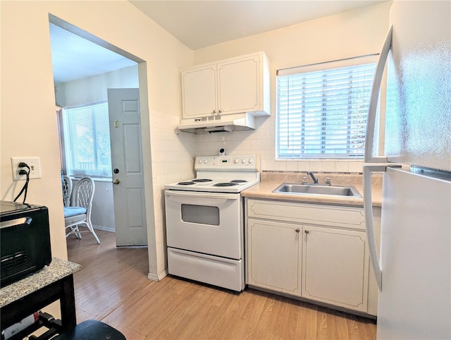 kitchen featuring under cabinet range hood, a healthy amount of sunlight, white appliances, and a sink