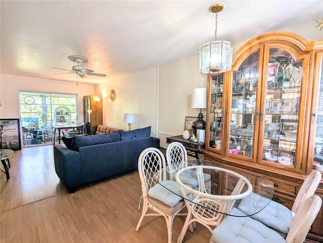 dining space featuring light wood-style flooring and ceiling fan with notable chandelier
