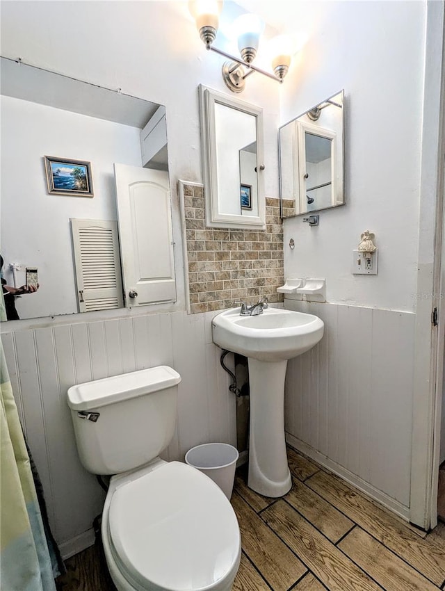 bathroom with toilet, wood finished floors, a wainscoted wall, and a sink