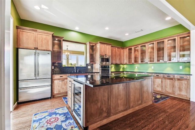 kitchen featuring beverage cooler, backsplash, built in appliances, light hardwood / wood-style floors, and a kitchen island