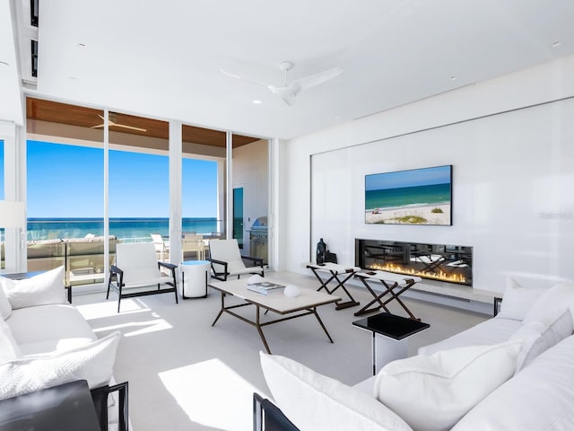 living room with expansive windows, carpet, a glass covered fireplace, and a ceiling fan