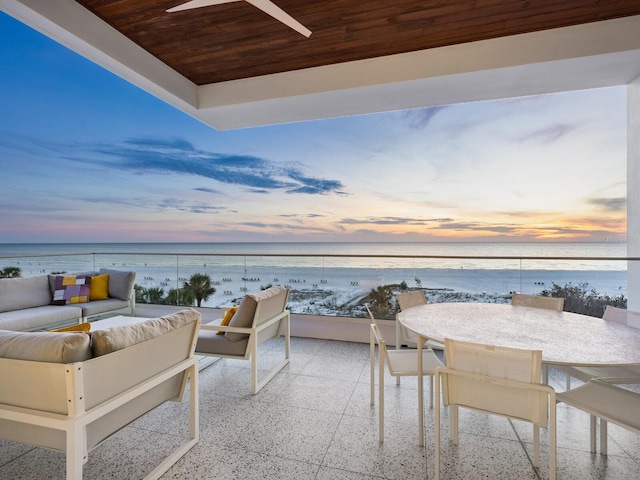 patio terrace at dusk with a beach view, outdoor lounge area, a water view, and a balcony