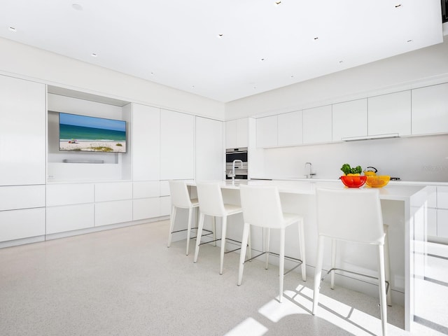 kitchen with light countertops, white cabinets, a kitchen bar, and modern cabinets