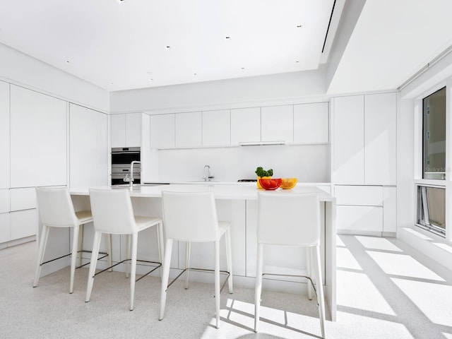 kitchen with double oven, a sink, white cabinetry, a kitchen breakfast bar, and modern cabinets