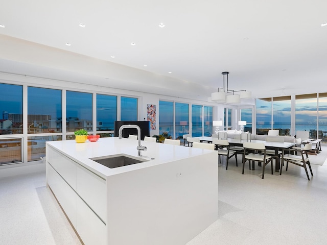 kitchen featuring a kitchen island with sink, a sink, white cabinetry, a wall of windows, and modern cabinets