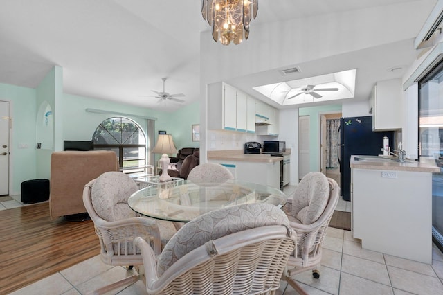 tiled dining area featuring lofted ceiling with skylight and ceiling fan with notable chandelier