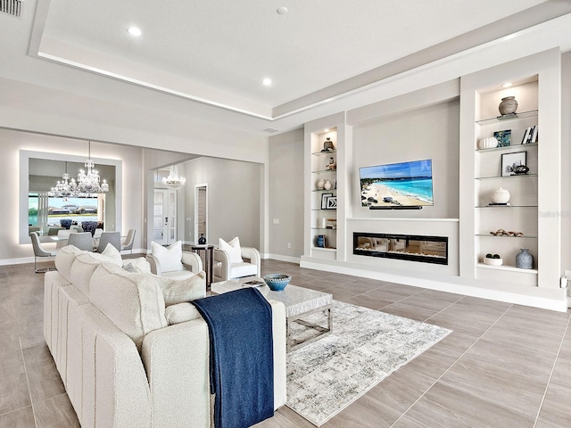 living room featuring a tray ceiling, built in shelves, and a notable chandelier