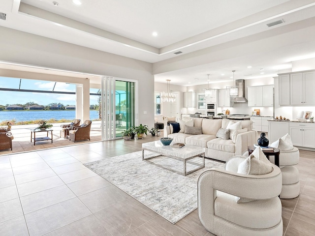 tiled living room with a notable chandelier, a water view, and a tray ceiling