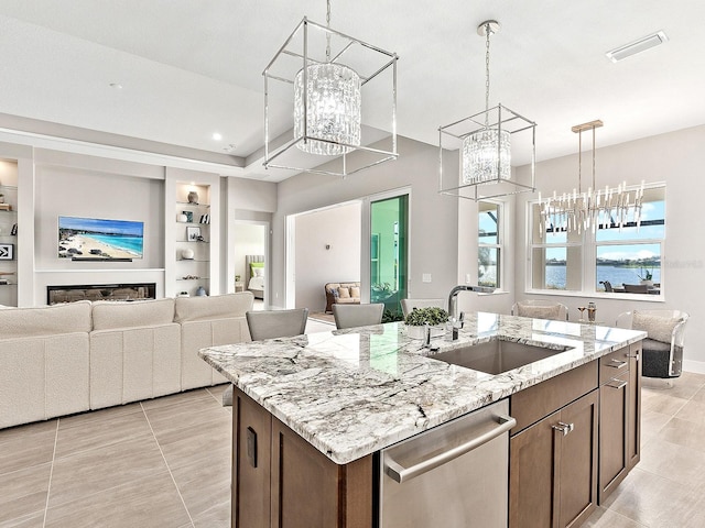 kitchen featuring light stone counters, stainless steel dishwasher, built in shelves, sink, and a center island with sink