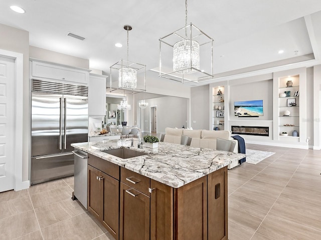 kitchen with built in shelves, sink, an island with sink, white cabinets, and appliances with stainless steel finishes