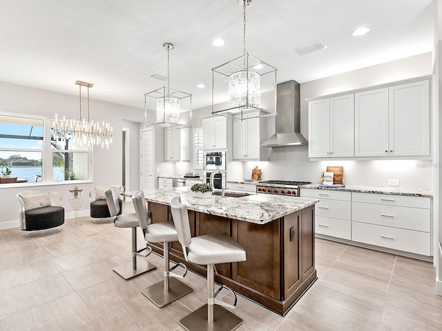 kitchen featuring hanging light fixtures, wall chimney range hood, a water view, a center island with sink, and white cabinets