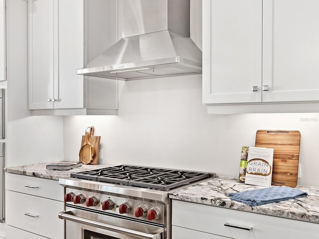 kitchen with white cabinets, high end stainless steel range oven, light stone countertops, and wall chimney range hood