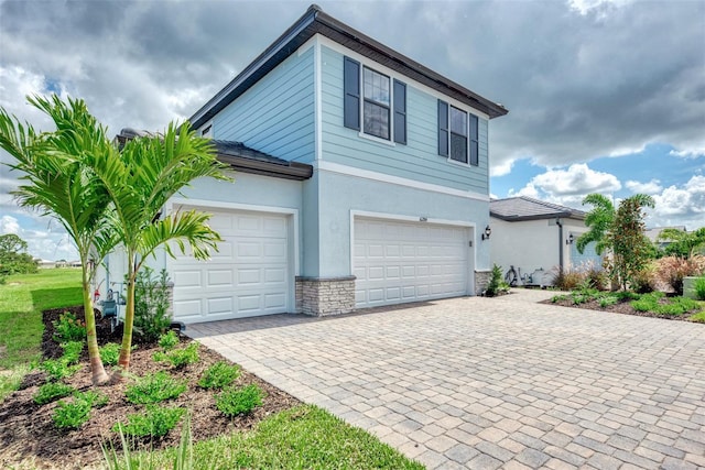 view of side of home with a garage, stone siding, decorative driveway, and stucco siding