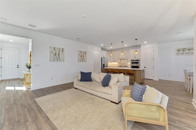 living room with light wood-style flooring, visible vents, baseboards, and recessed lighting