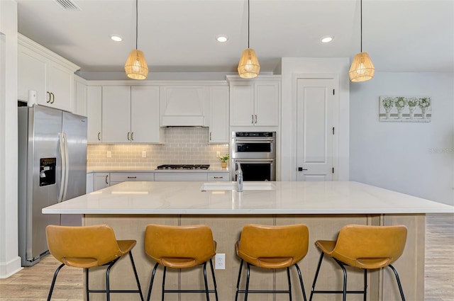 kitchen featuring light wood finished floors, tasteful backsplash, appliances with stainless steel finishes, white cabinetry, and premium range hood