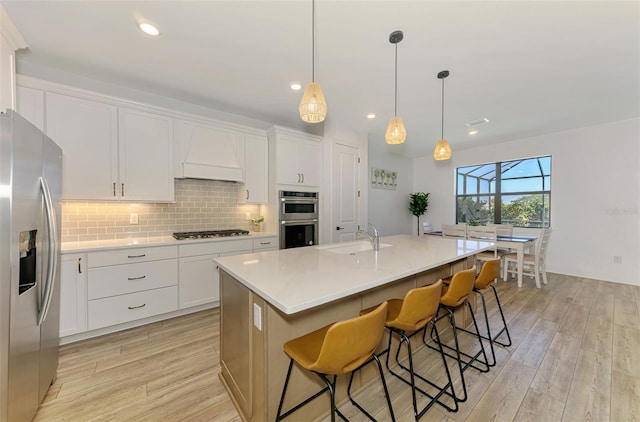 kitchen with a sink, appliances with stainless steel finishes, light wood-type flooring, backsplash, and custom range hood