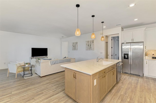 kitchen with light wood-style flooring, a sink, open floor plan, appliances with stainless steel finishes, and decorative backsplash