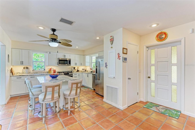 kitchen with white cabinetry, ceiling fan, stainless steel appliances, a kitchen bar, and light tile patterned floors