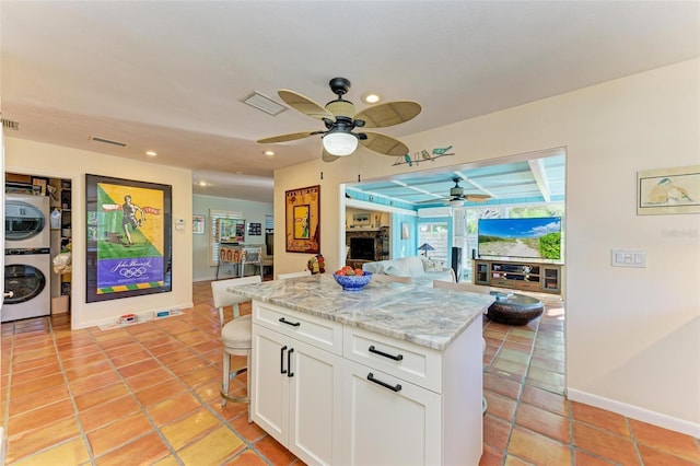 kitchen with a kitchen bar, light stone counters, stacked washer / dryer, white cabinets, and a center island