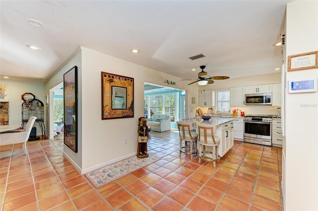 kitchen featuring appliances with stainless steel finishes, a kitchen breakfast bar, ceiling fan, white cabinets, and a kitchen island