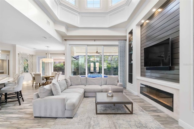 living room with a high ceiling, light hardwood / wood-style floors, crown molding, and built in shelves